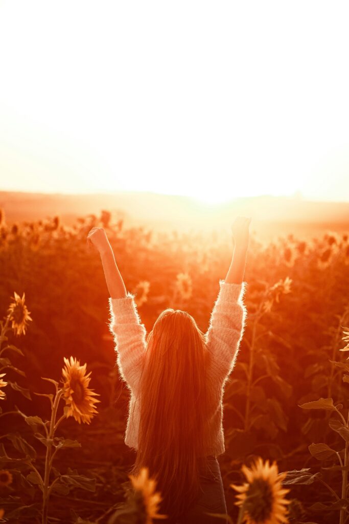 Woman stands in a sunflower field at sunset, exuding joy and freedom.