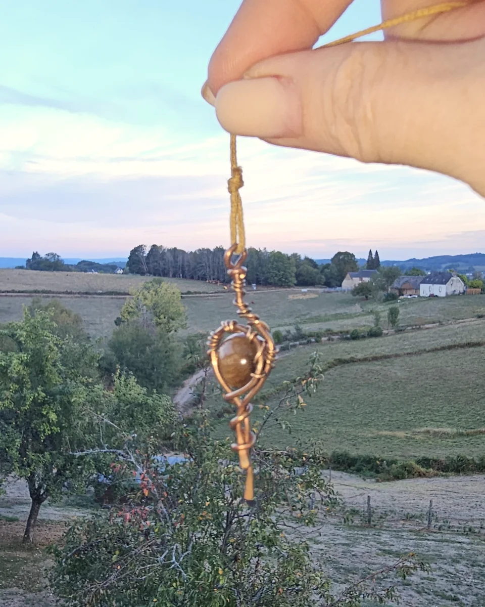 Pendule en œil-de-tigre tenu devant la campagne corrézienne au crépuscule